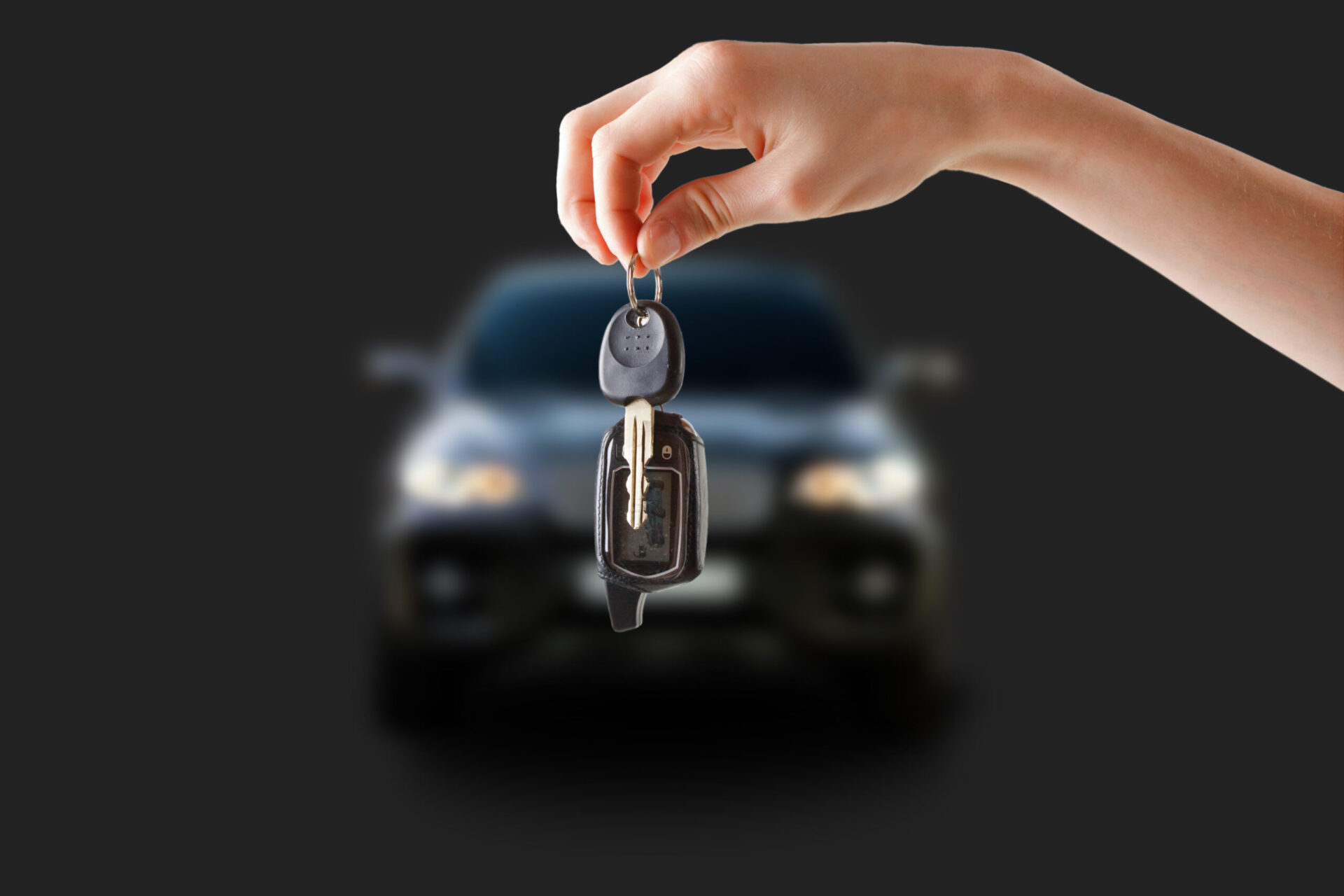 A hand holding a car key fob and traditional metal key in the foreground, with a blurred car in the background against a dark, neutral backdrop. The image conveys themes of car rental.